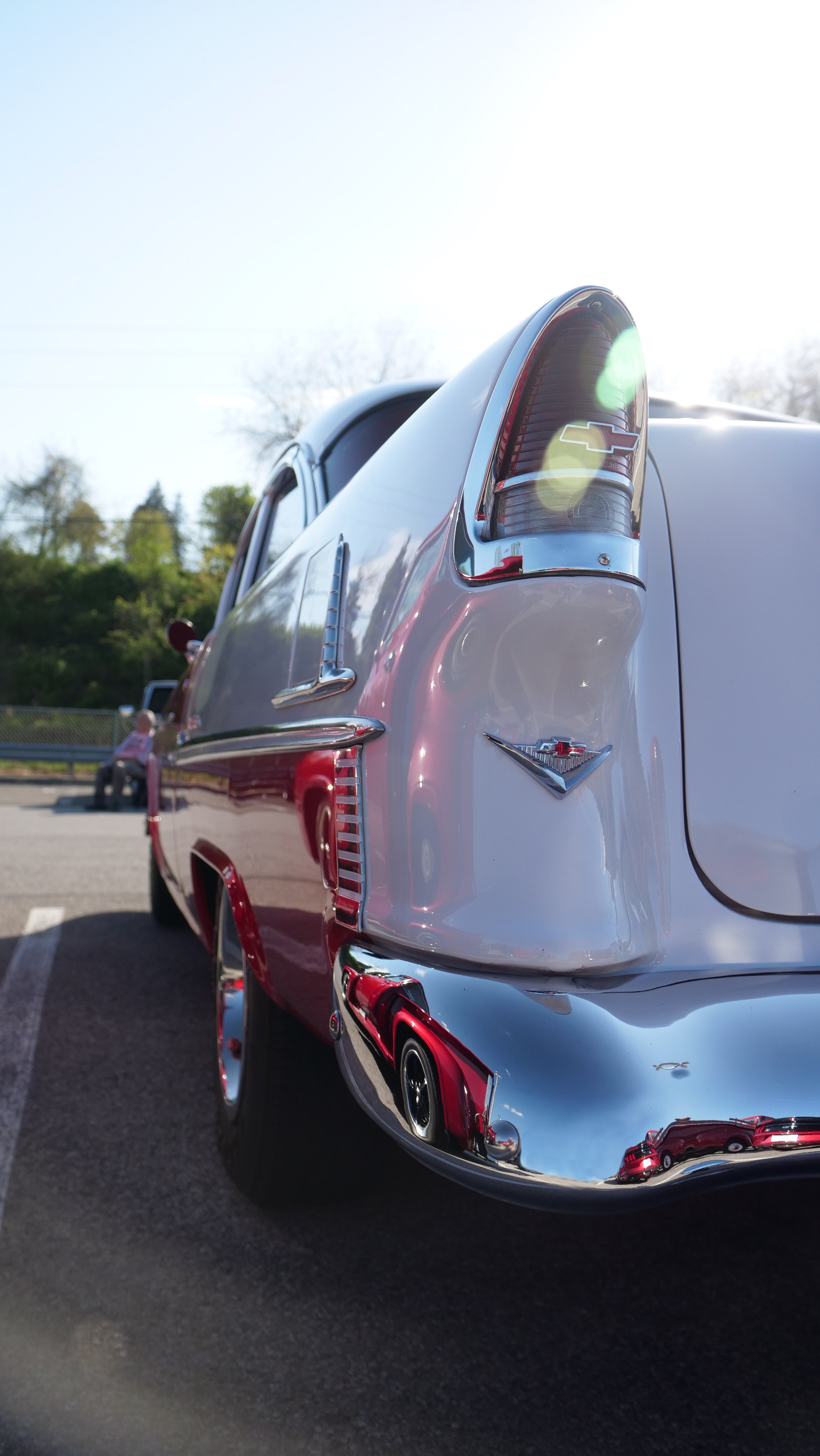 Close-up of the rear of a vintage Chevrolet car with chrome details and a Chevrolet emblem, parked outdoors on a sunny day.