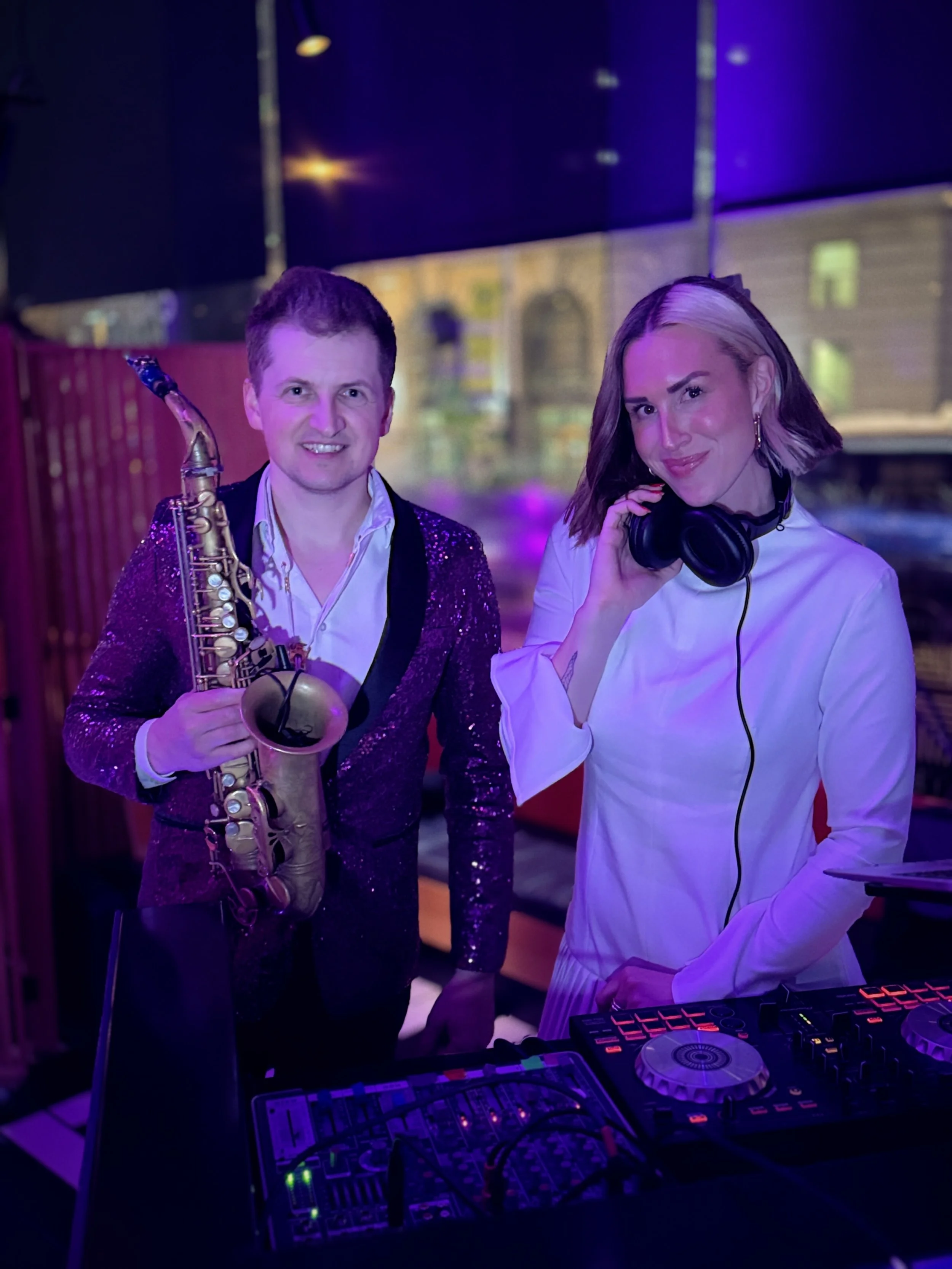 Rachel Molenda wearing white outfit DJ-ing at brand activation posing with man in a suit with a saxophone
