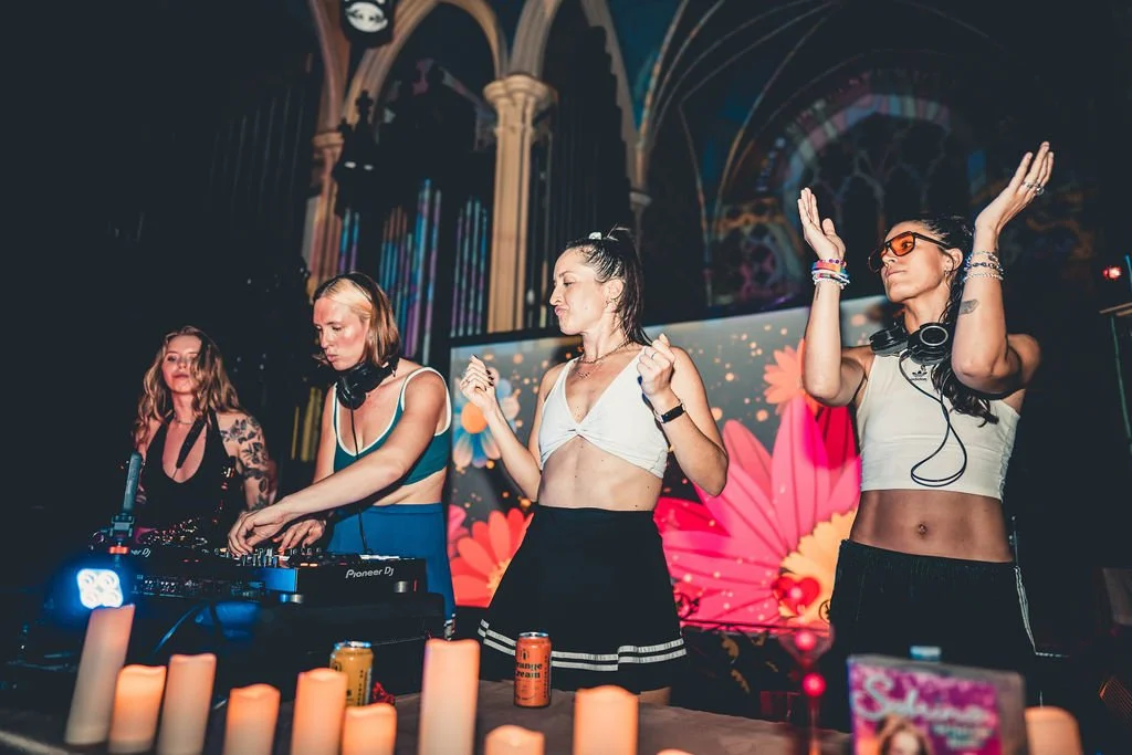 Rachel Molenda wearing blue cheerleading uniform with friends behind the DJ booth DJ-ing and MC-ing at REUNION Dance party event