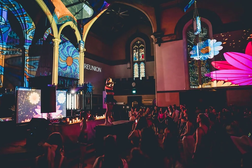 Rachel Molenda wearing blue cheerleading uniform performing and MC-ing at REUNION Dance party event with women dancing in the crowd