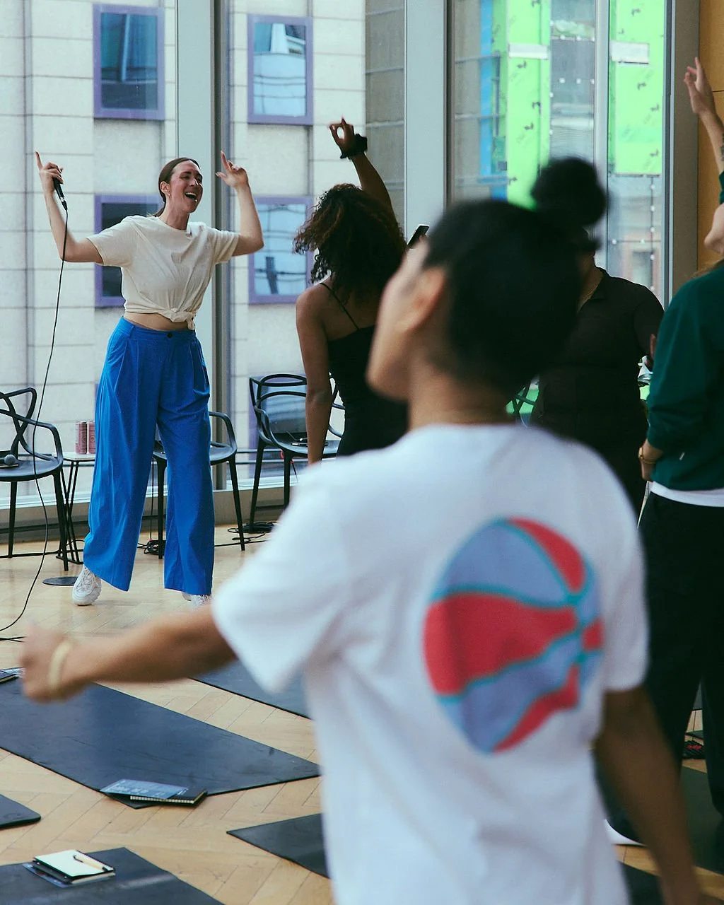 Rachel Molenda wearing blue pants and white tshirt on a microphone MC-ing at brand activation with women dancing in the audience