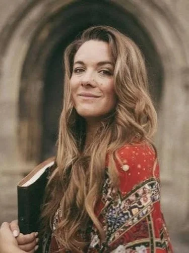 Sarah Jenks posing wearing a red patterned robe and holding a book