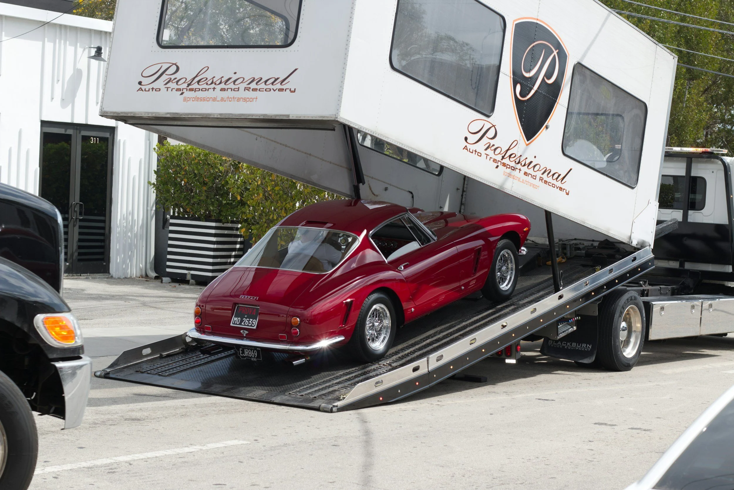 A red classic car being transported on a car carrier truck with the logo 'Professional Auto Transport and Recovery'.