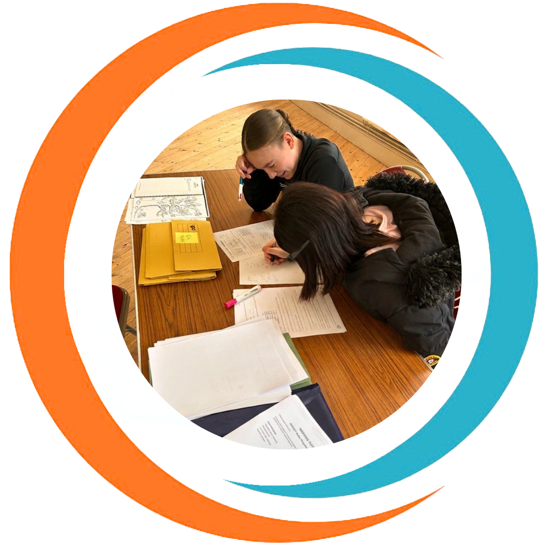 Two students sitting at a wooden table, studying with notebooks, papers, and folders.