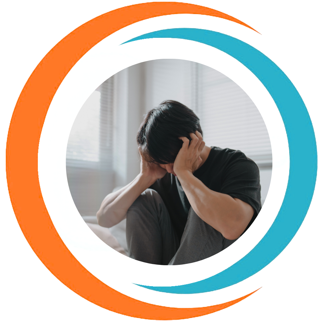 A person sitting on a bed holding their head in their hands, appearing distressed or anxious, with window blinds in the background.