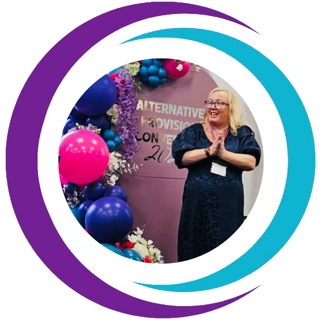 Woman smiling with hands together at a conference with colorful balloons and flowers, backdrop reads 'ALTERNATIVE PROVISION CONFERENCE 2022'.