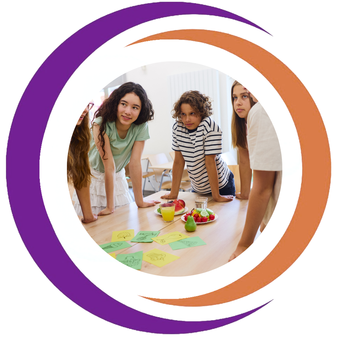 Group of children gathered around a table with colorful fruits and drawings, engaging in a discussion or activity.