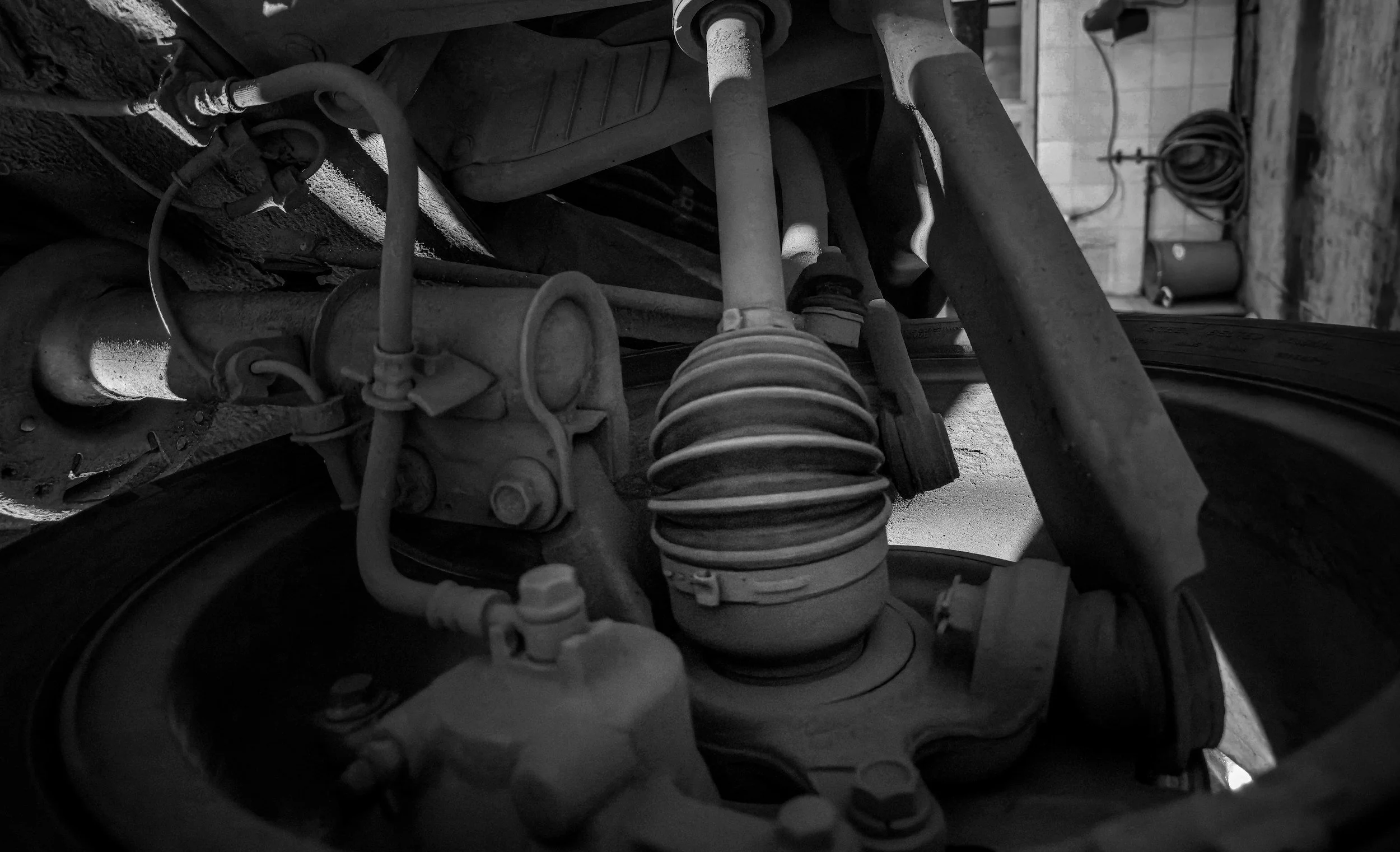 Black and white photo of car suspension components, including coil spring, shock absorber, and various rods and wires.