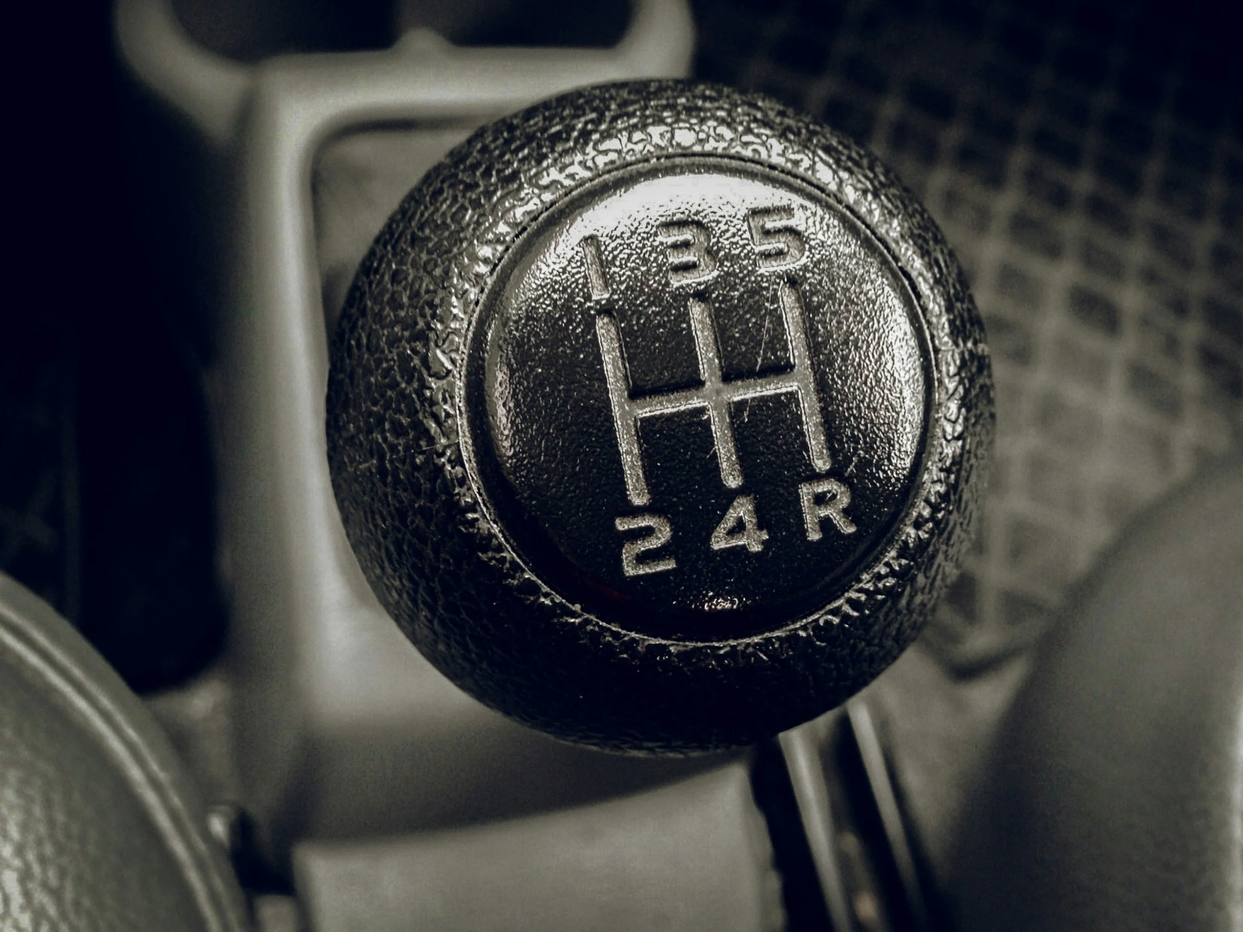 Close-up of a manual gear shift knob in a car, showing the shift pattern with the numbers 1, 3, 5, 2, 4 and the letter R for reverse.