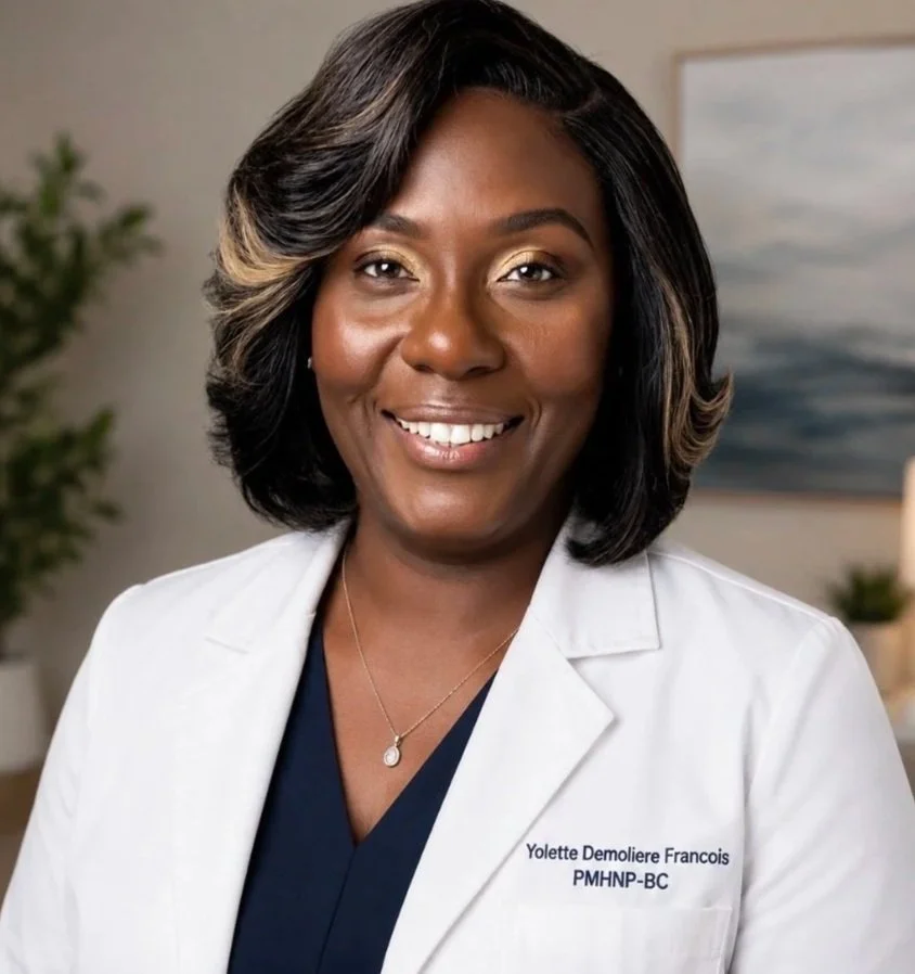 Smiling woman in medical coat with name tag that reads Yolette Demoliere Francois, PMHNP-BC, in a professional setting