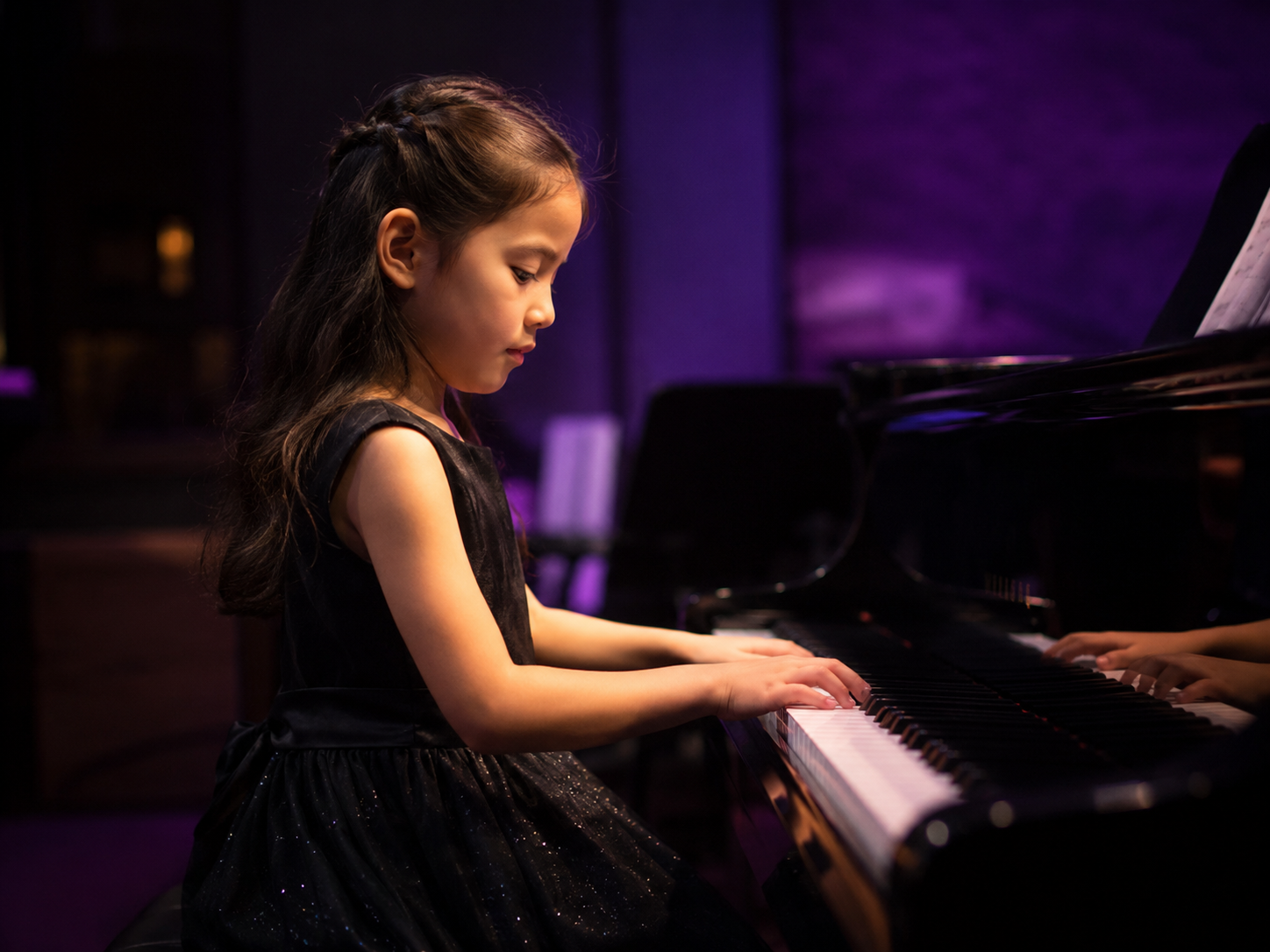 A young girl playing the piano in a dimly lit room with purple lighting.