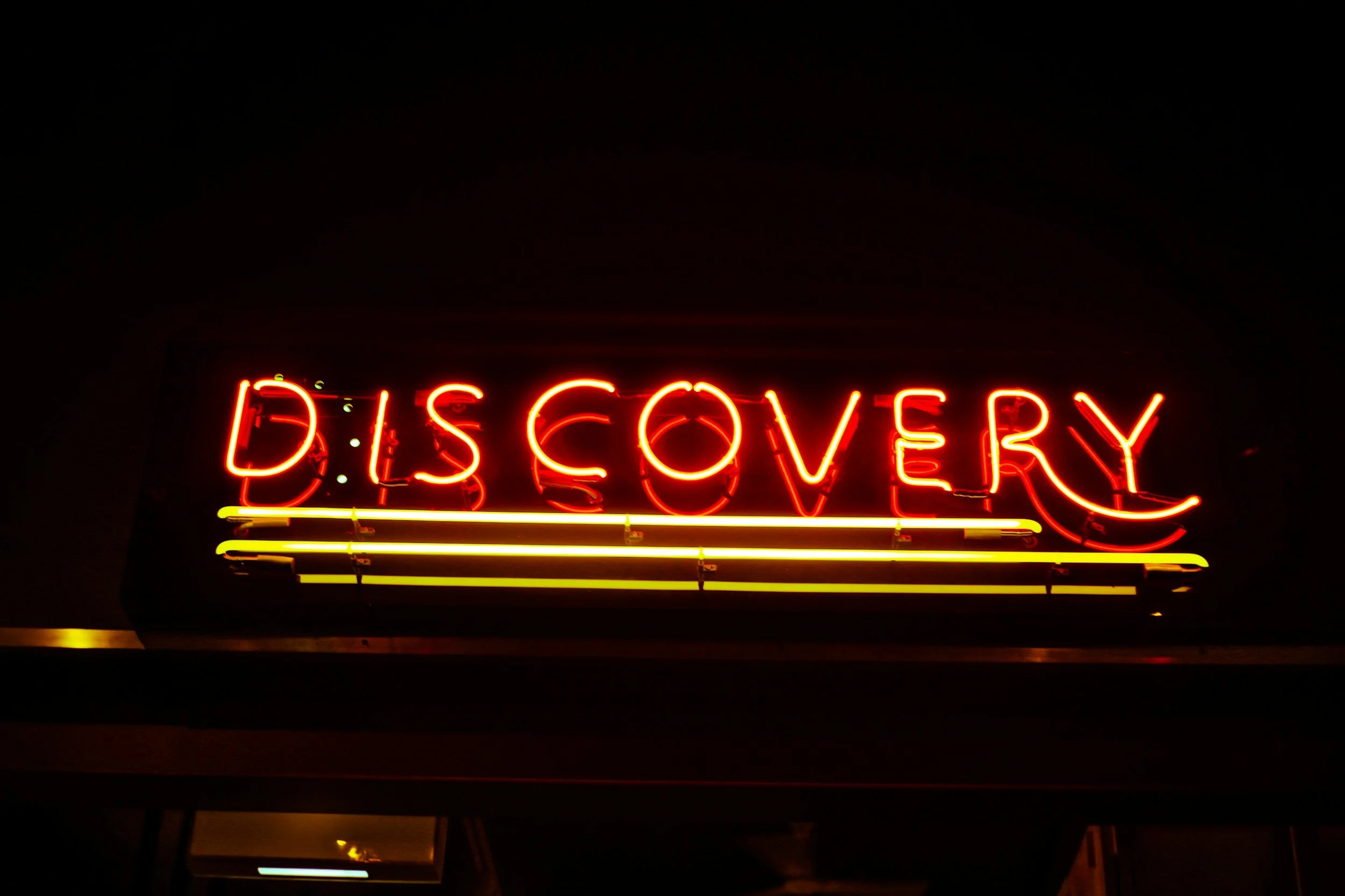 Neon sign displaying the word "DISCOVERY" in red and yellow lights against a dark background.