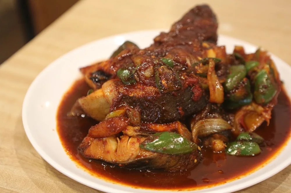 A plate of cooked fish topped with a spicy tomato-based sauce with vegetables and herbs.