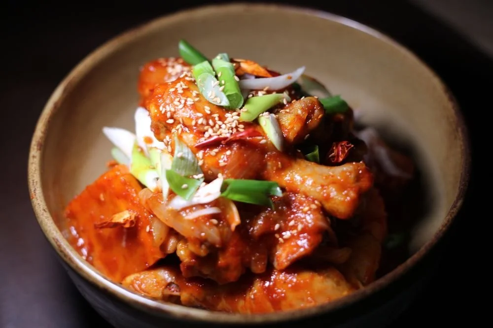 A bowl of spicy Korean chicken stir-fry garnished with chopped green onions and sesame seeds.