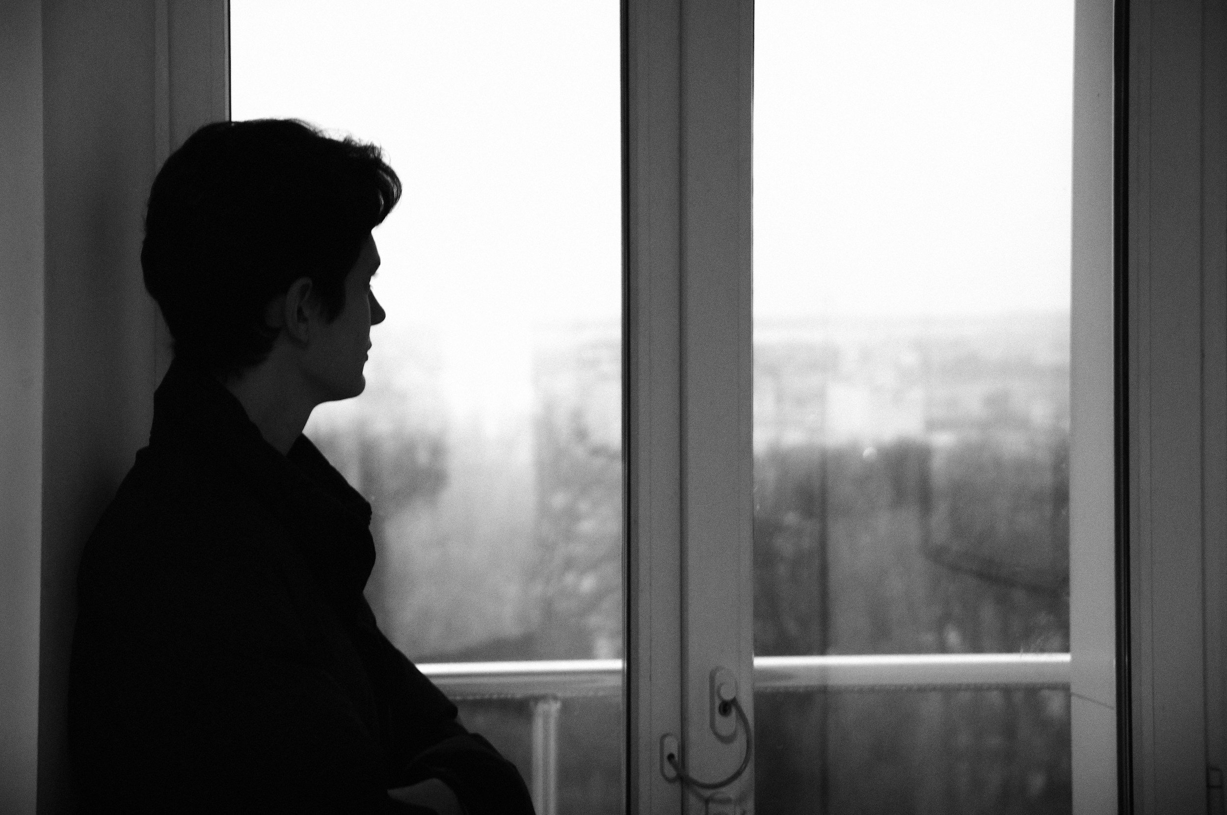 Ein silhouettierter Mensch sitzt vor einem Fenster, Blick nach draußen, in einem schwarz-weißen Bild.