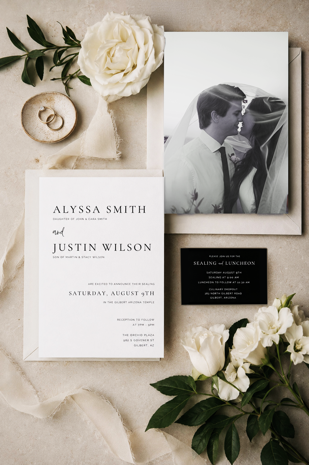 Wedding invitation suite with couple's photo, rings, white flowers, and event details on a neutral background.