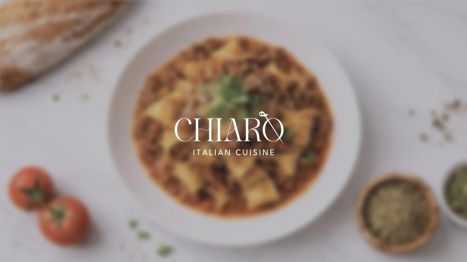 A top-down view of a pizza topped with cheese, meat, and herbs on a white plate. There are cherry tomatoes and small bowls of dips or sauces around it. The text overlay reads "Chiaro Italian Cuisine."