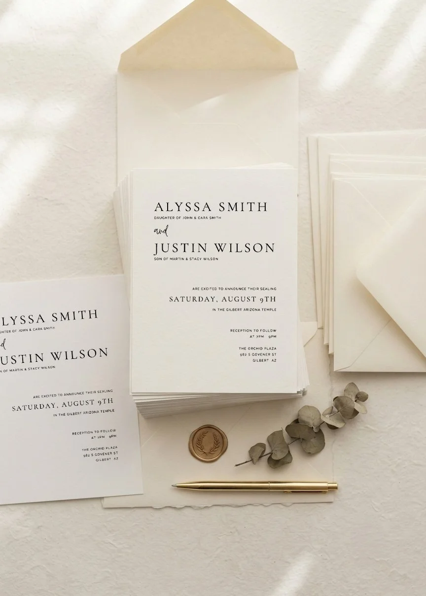 Wedding invitation suite with white cards, an envelope, a wax seal, a sprig of eucalyptus, and a gold pen.