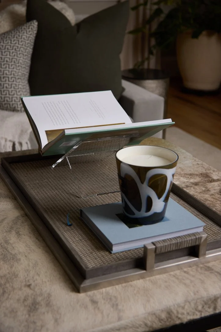 A tray with a book stand, an open book, a closed book, and a cup of coffee on a textured tray on a beige sofa.