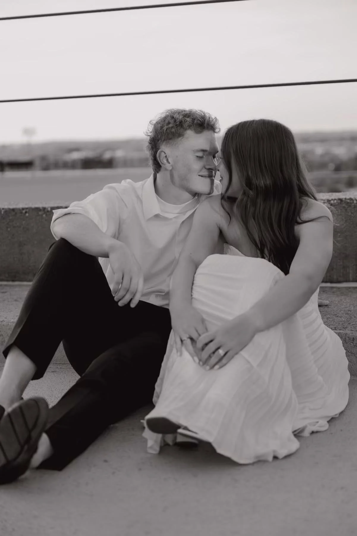 A young couple sitting on the ground, close together with their foreheads touching and eyes closed, sharing an intimate moment.