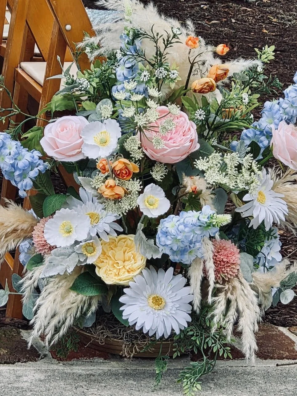 A colorful floral arrangement with pink, white, yellow, and blue flowers, including roses, daisies, and other blooms, placed in a basket.