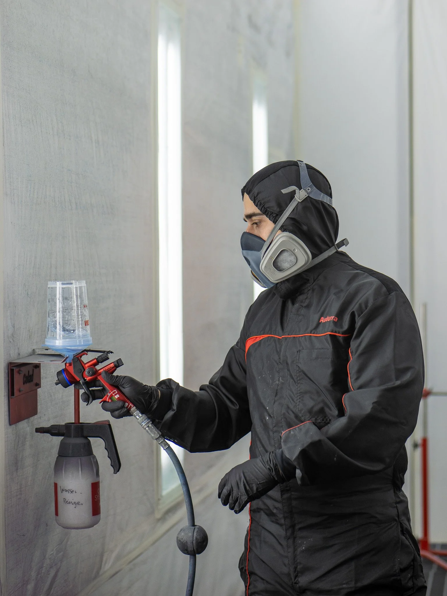 Ein Mann trägt Schutzmaske, Handschuhe und eine schwarze Jacke, während er in einem Labor mit einem Rotationsverdampfer arbeitet. Der Mann ist seitlich sichtbar, und im Hintergrund sind weiße Wandflächen und eine Beleuchtung zu sehen.