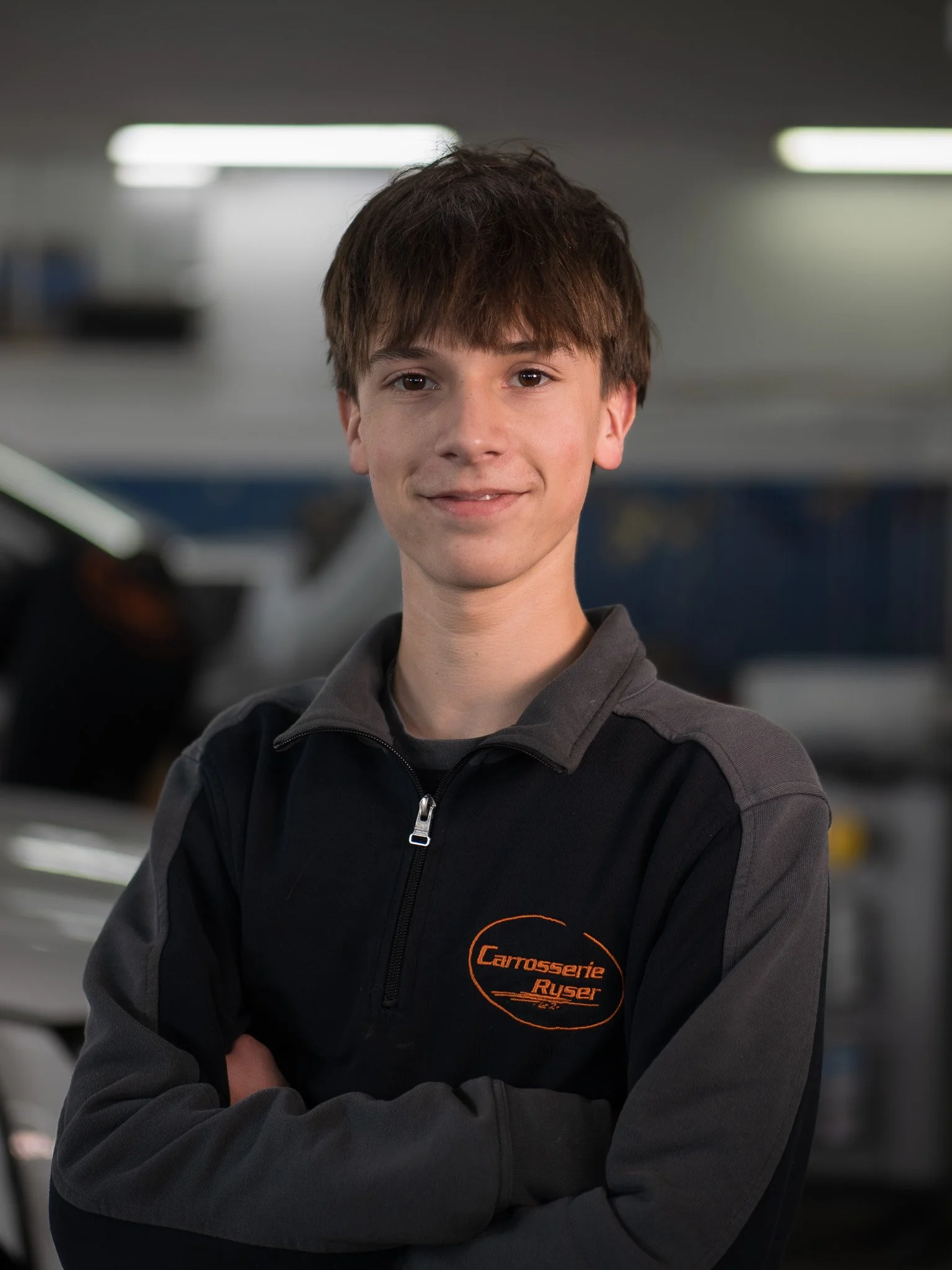 Junge Person in Werkstatt mit Carrosserie Ruser Logo auf Jacke