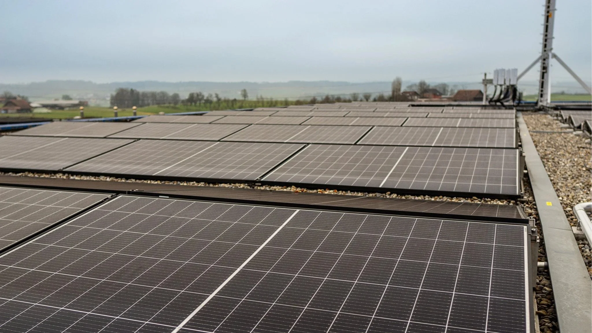 Dach mit Solarpanelen auf einer modernen Immobilie, mit einer ländlichen Landschaft im Hintergrund, bewölkter Himmel.