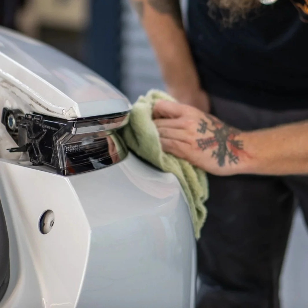 Hand eines Mechanikers, der eine weiße Autolampe mit einem Tuch reinigt.