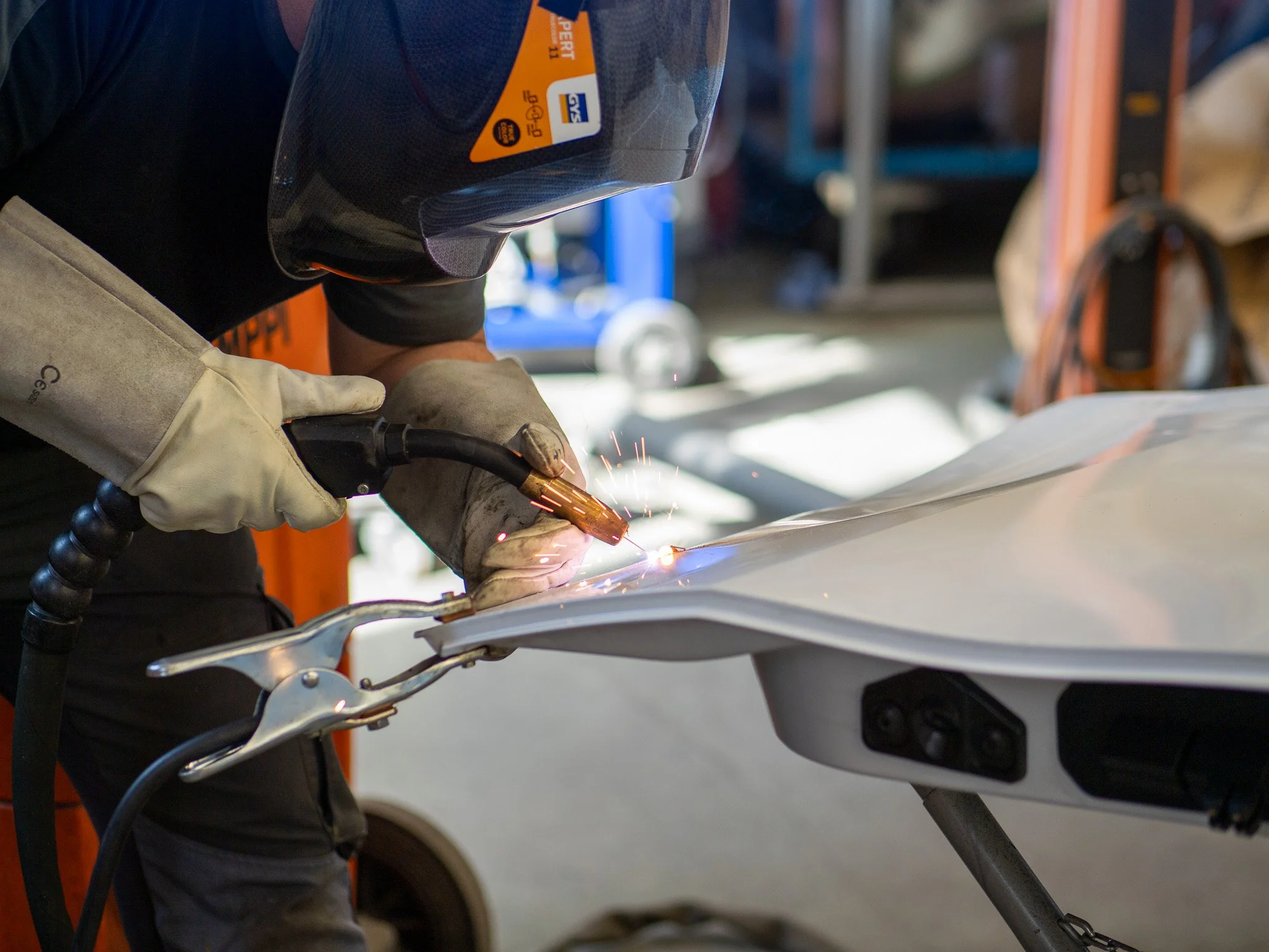 Person beim Schweißen eines Motorrads im Werkstattumfeld, trägt Schutzhelm und Handschuhe.