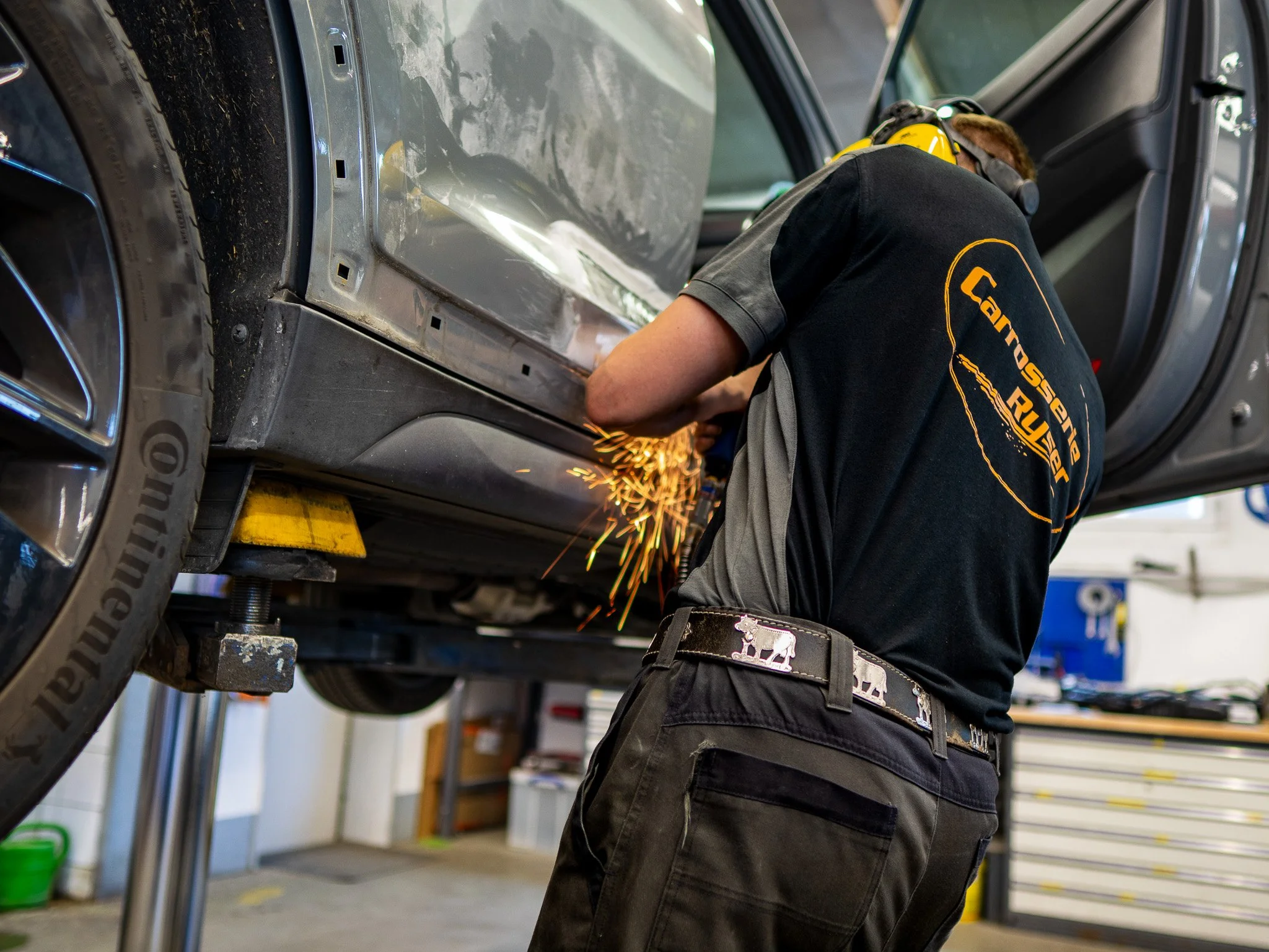 Ein Mechaniker arbeitet unter einem Auto, schweißt Metall und erzeugt Funken, während er in einer Werkstatt steht.