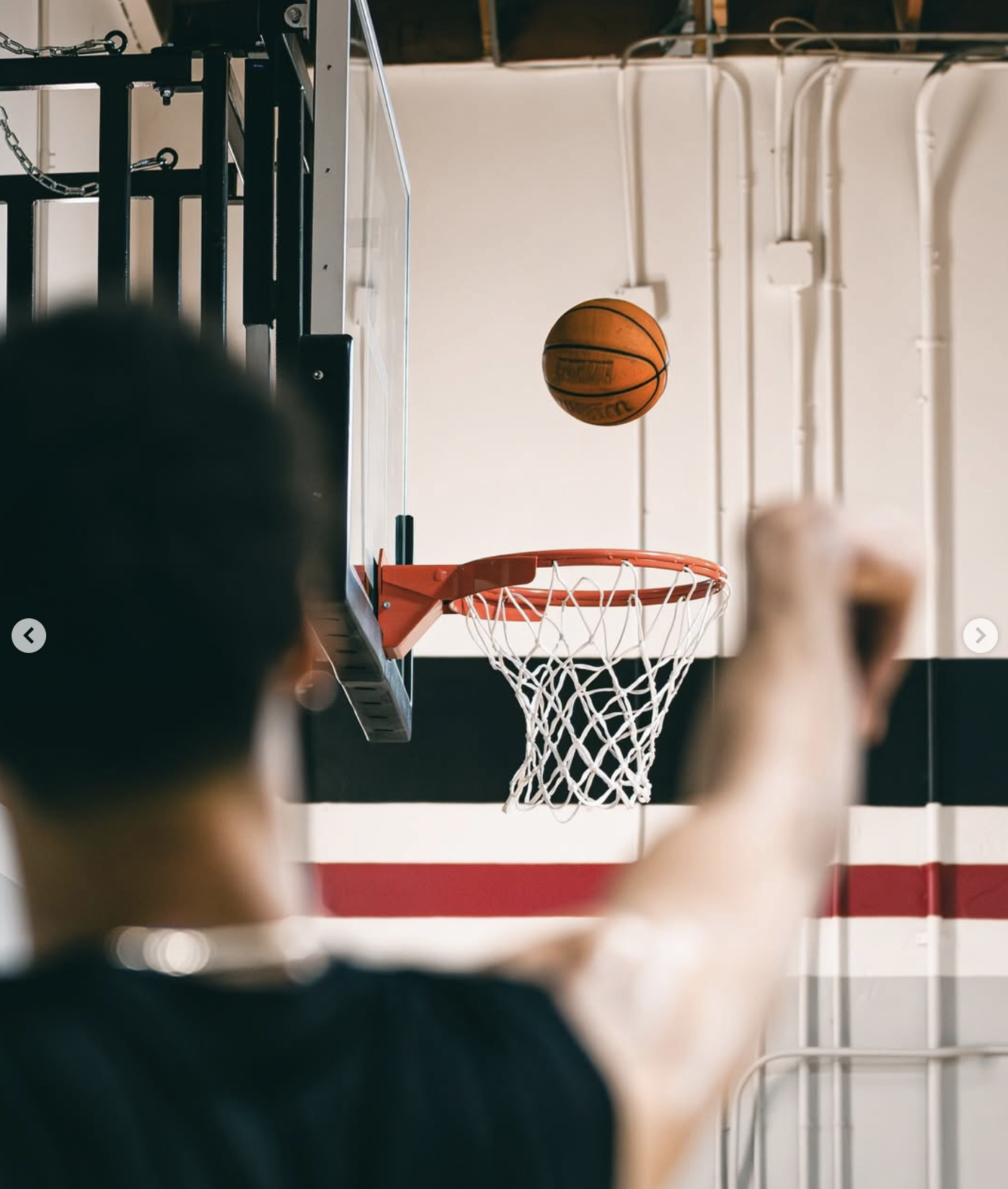 Child shooting a basketball towards a hoop in an indoor gym.