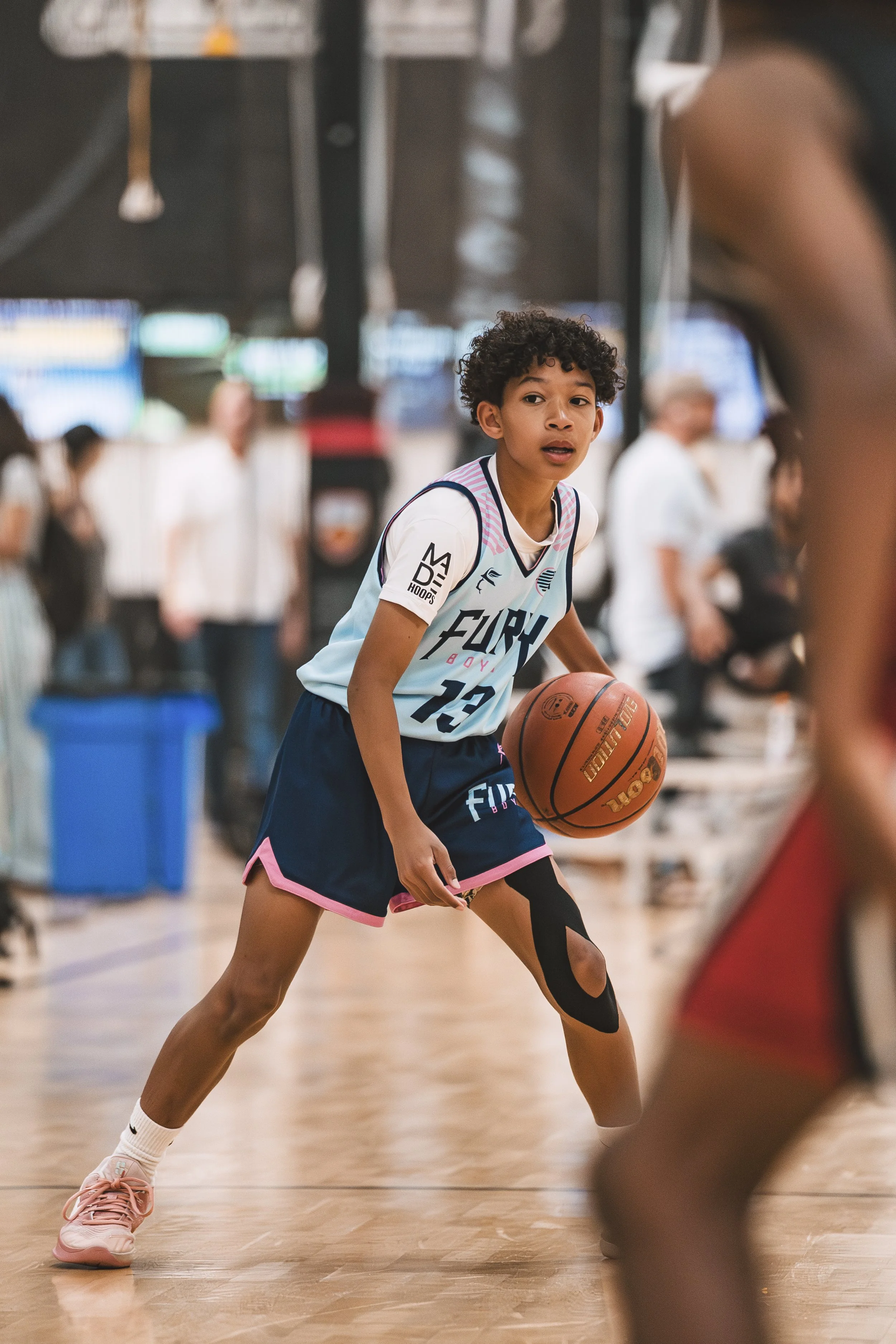 Young girl playing basketball on an indoor court, holding a basketball with her right hand, and wearing a basketball uniform with the number 12.