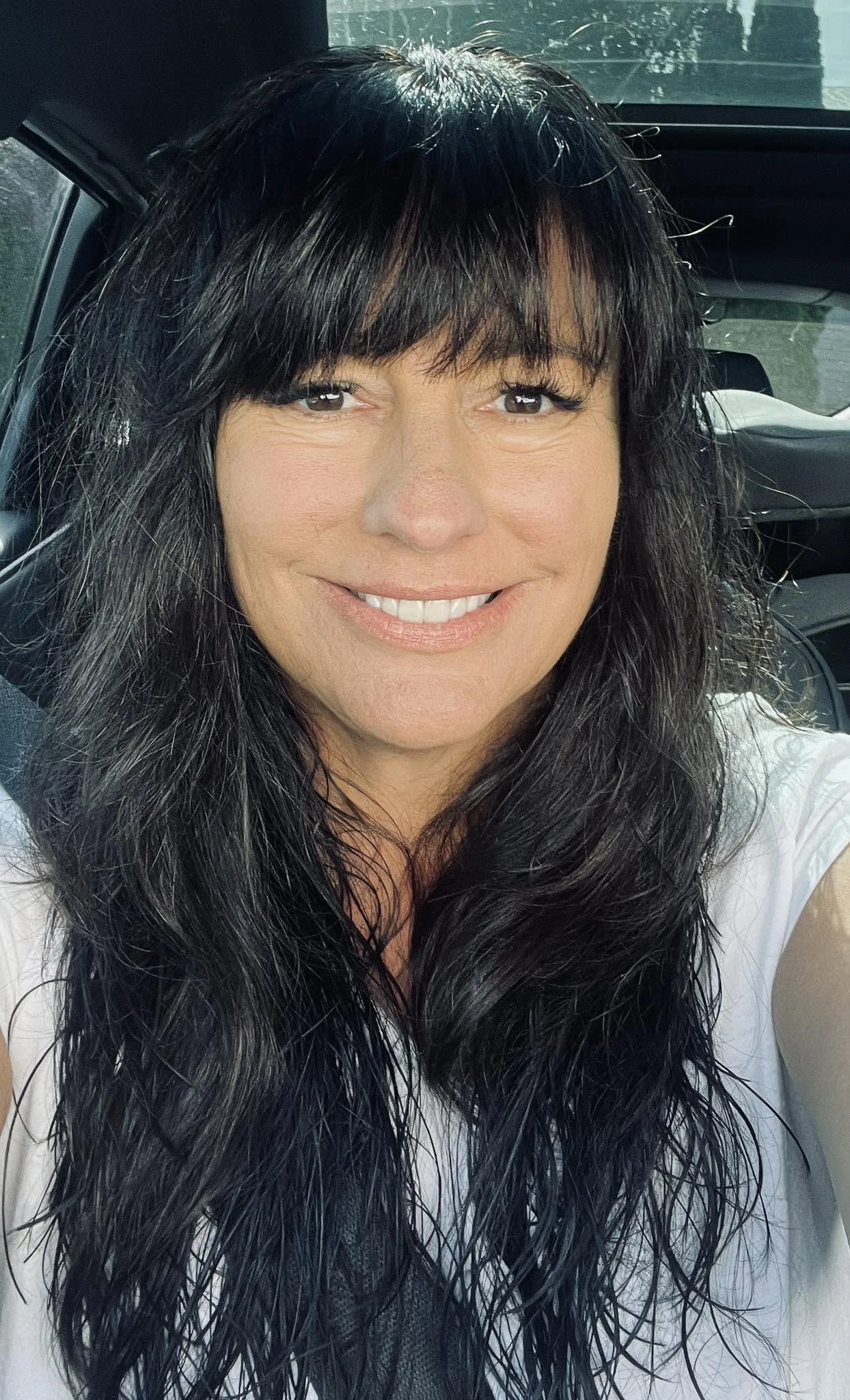 A woman with long, wet black hair and bangs, smiling inside a vehicle.