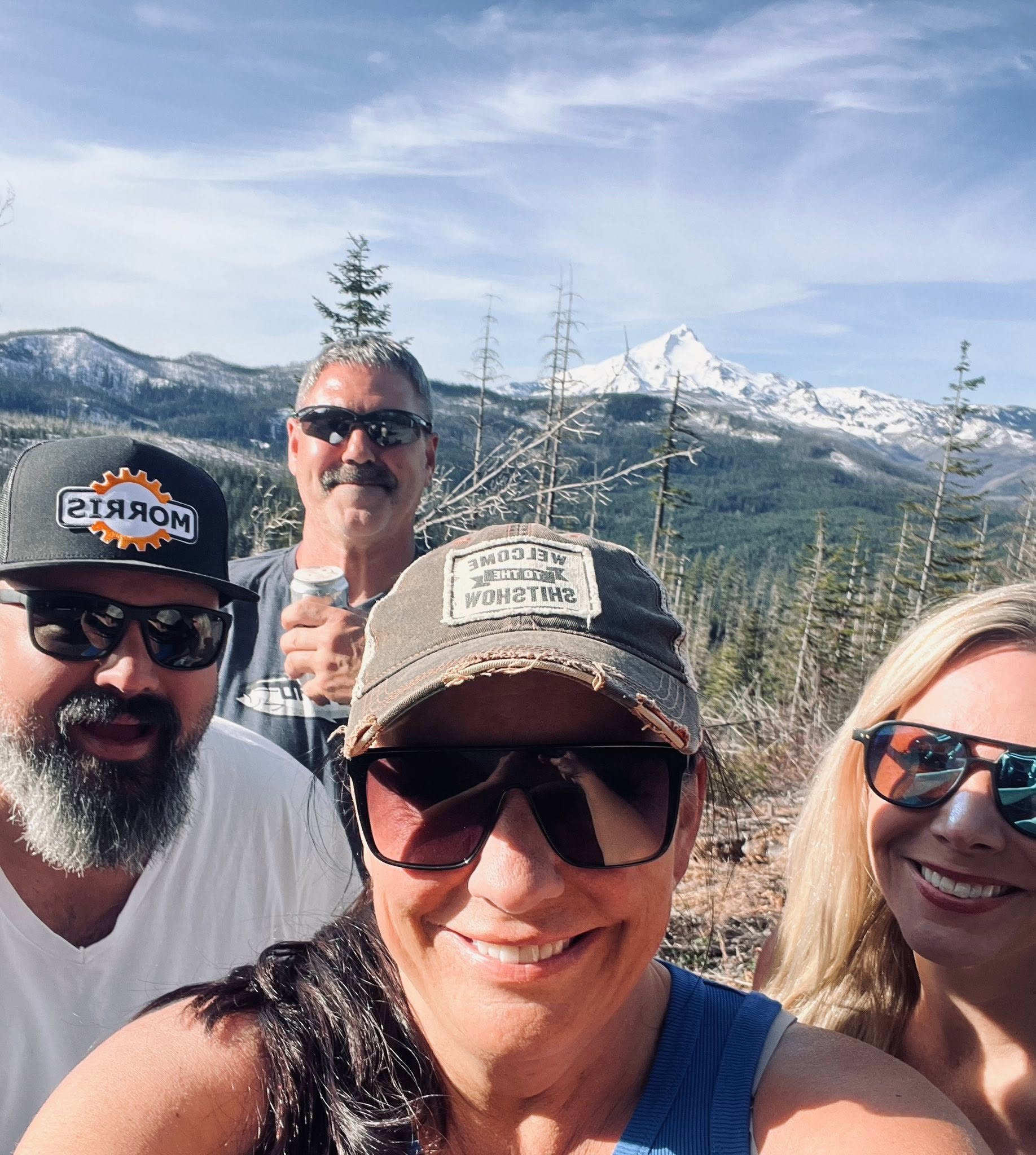 Group of people smiling outdoors with a mountain and blue sky in the background.