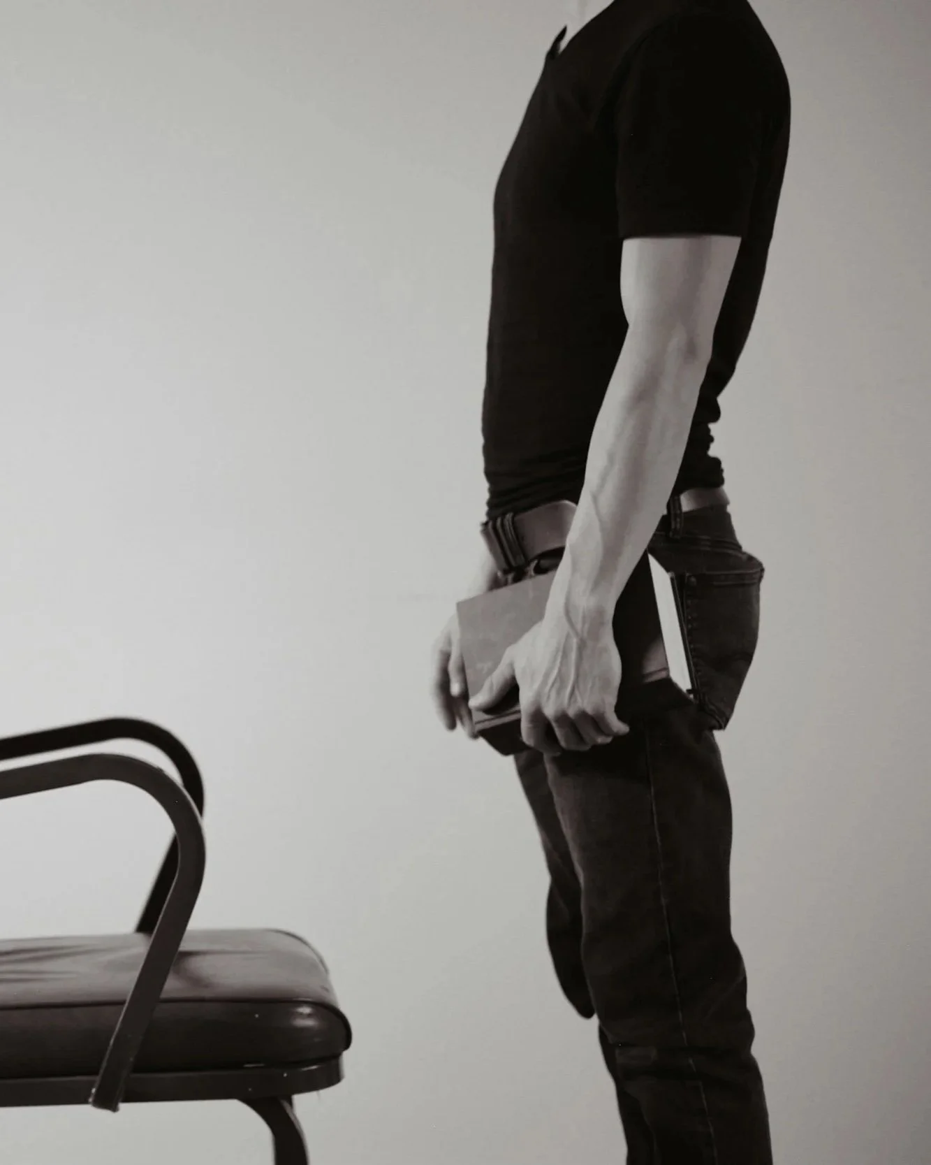 Person standing next to a chair, holding a book in their left hand.