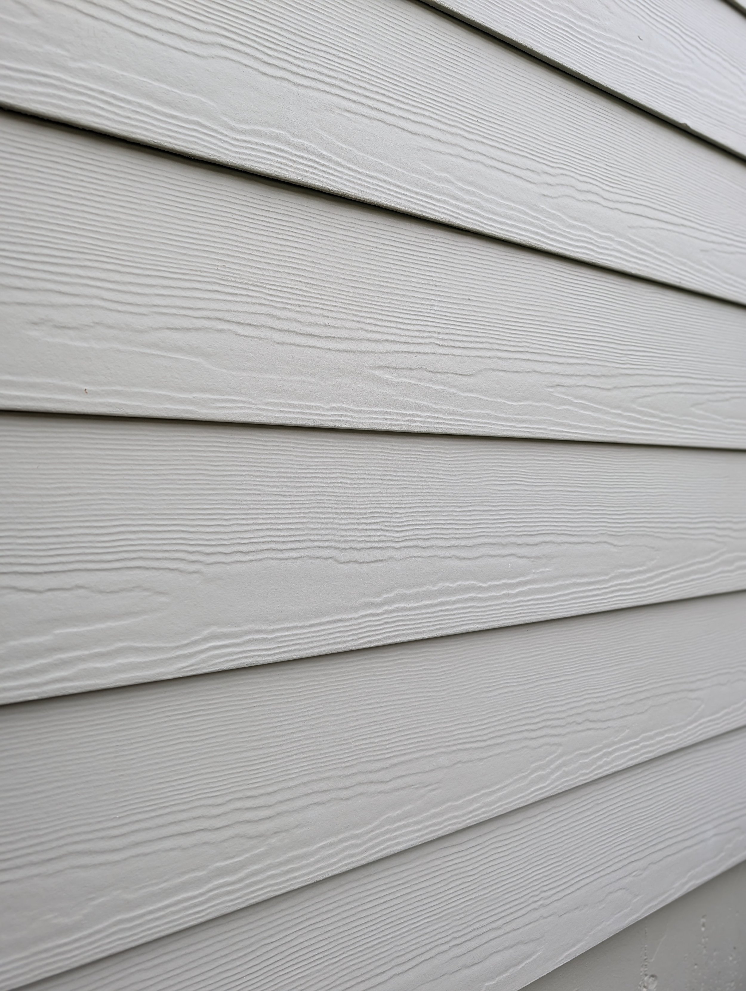 Close-up of horizontal white vinyl siding with textured wood grain pattern.