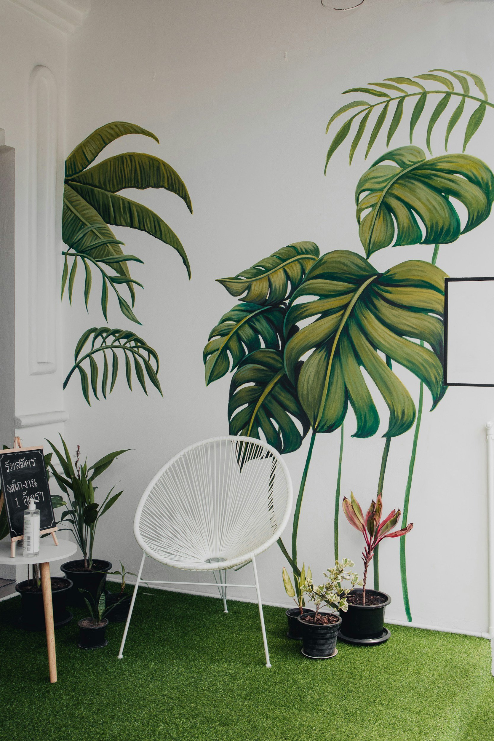 Example: hand-painted tropical botanical mural on a white interior wall, featuring large green leaves in a bright modern space.