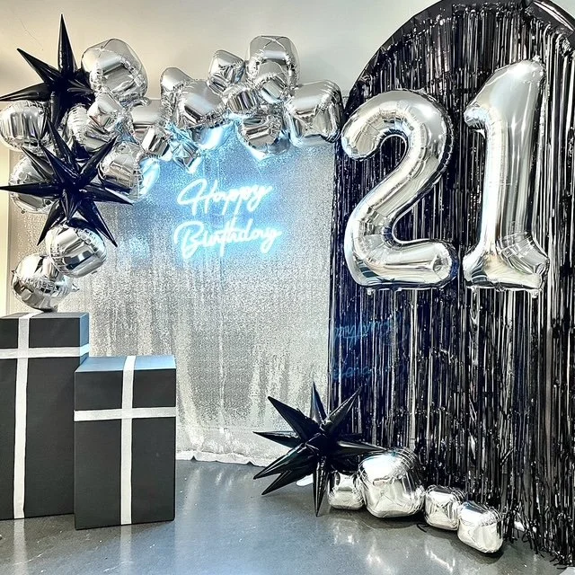 Birthday decoration with shiny balloons, presents, and a sign that says 'Happy Birthday' for a 21st celebration.
