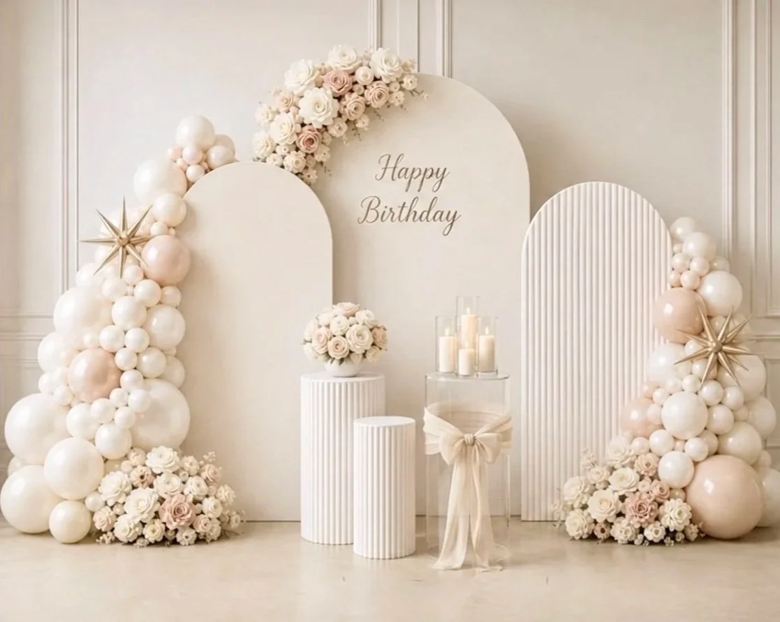 Elegant birthday decorating setup with white and blush balloons, floral arrangements, candles, and a