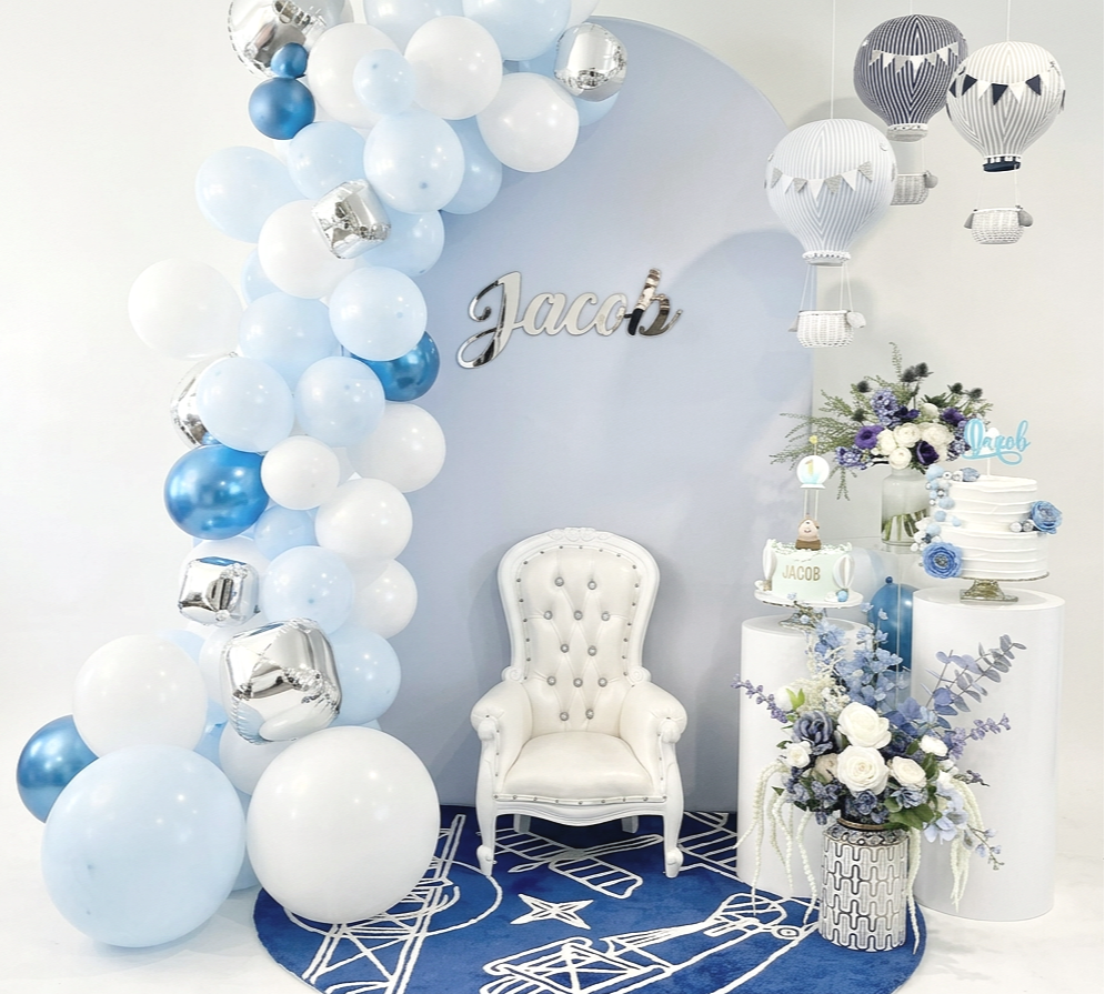 Decorative setup with blue and white balloons, a white armchair, hot air balloon decorations, and flowers for a celebration or party.