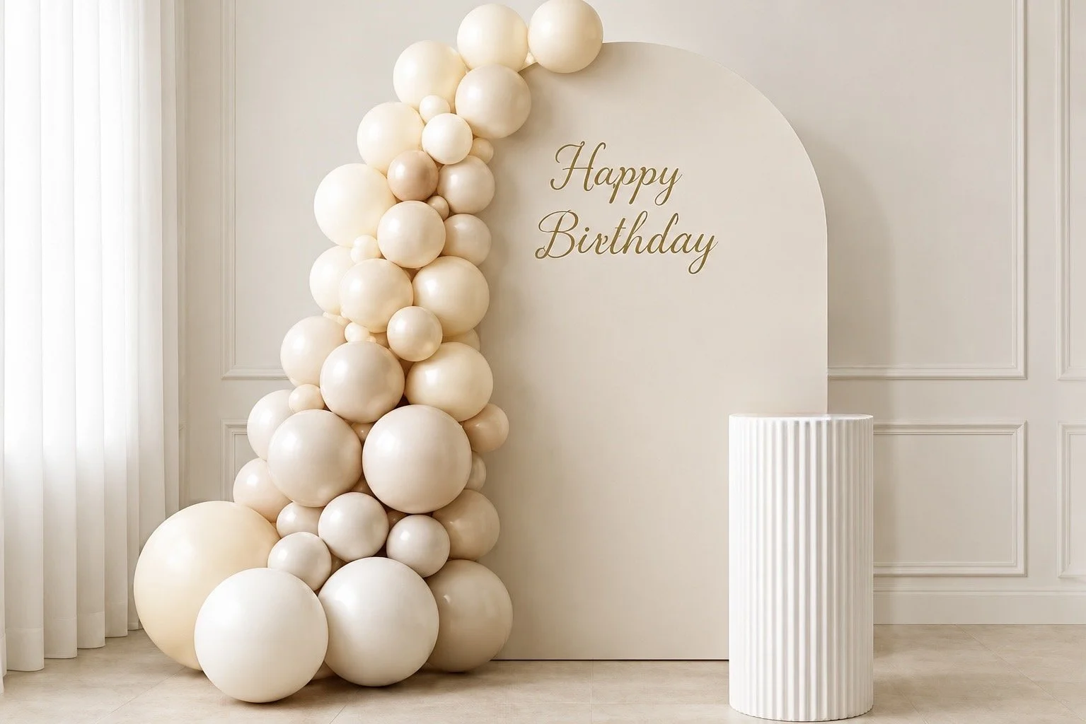 Cream-colored balloons arranged as a decoration next to a white wall with 'Happy Birthday' written in gold, standing in an elegant room.