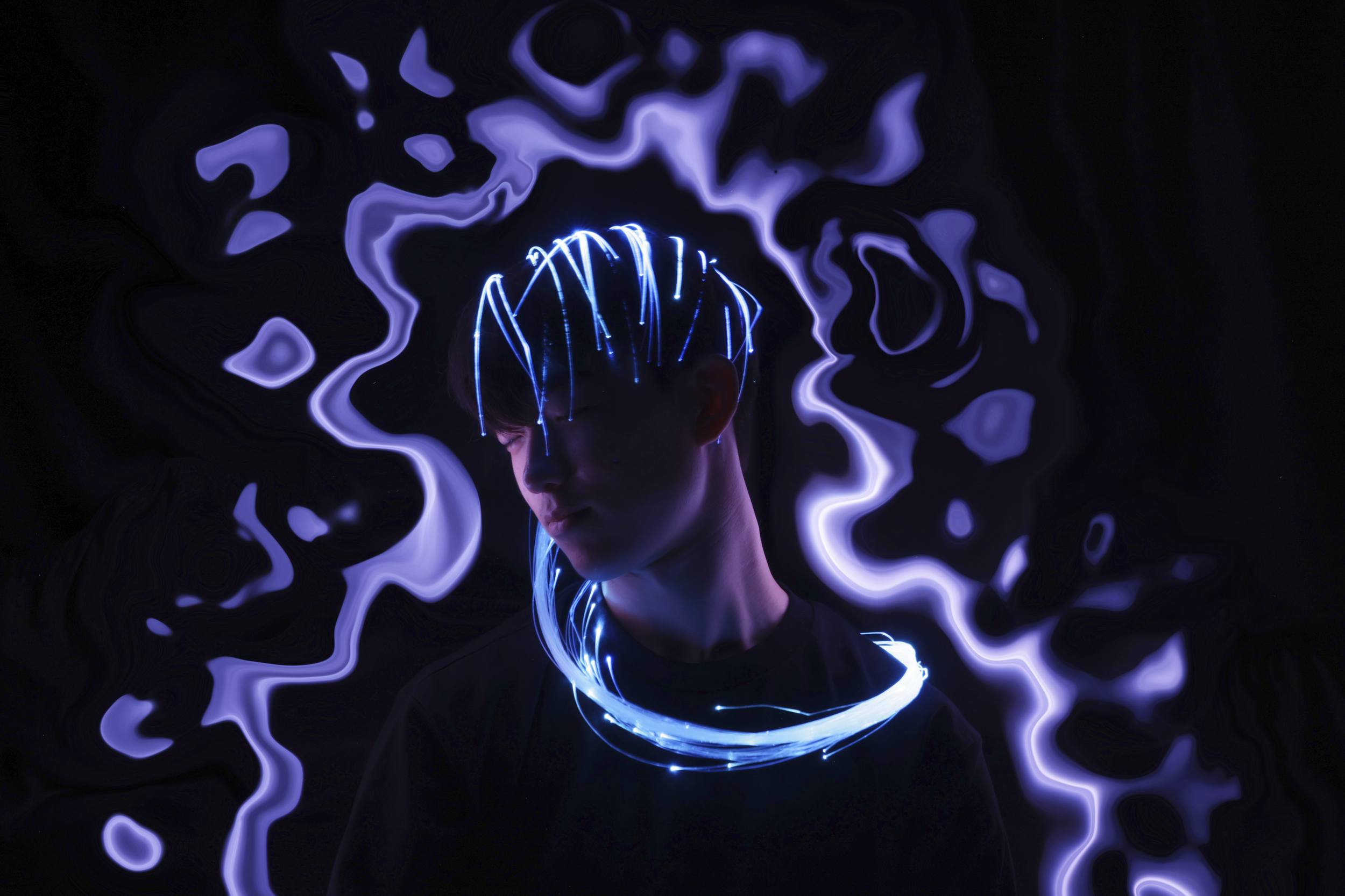A person with short hair wearing a black shirt, surrounded by glowing blue and purple electric-like light effects in a dark environment.