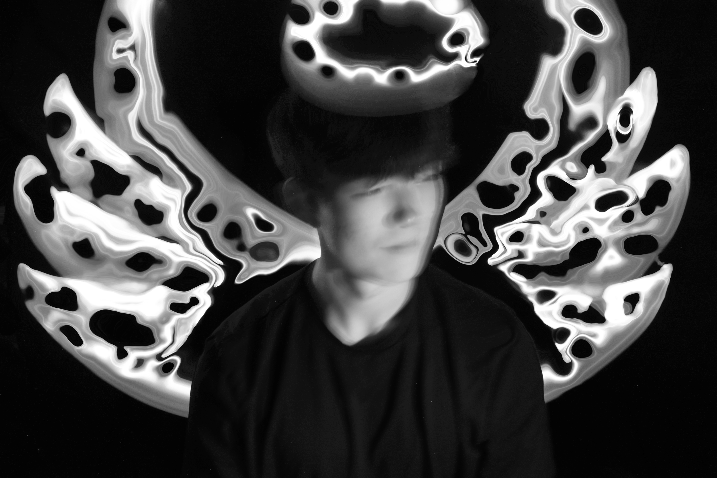 A person wearing a hat with an abstract black and white pattern, standing in front of a background with swirling light designs.