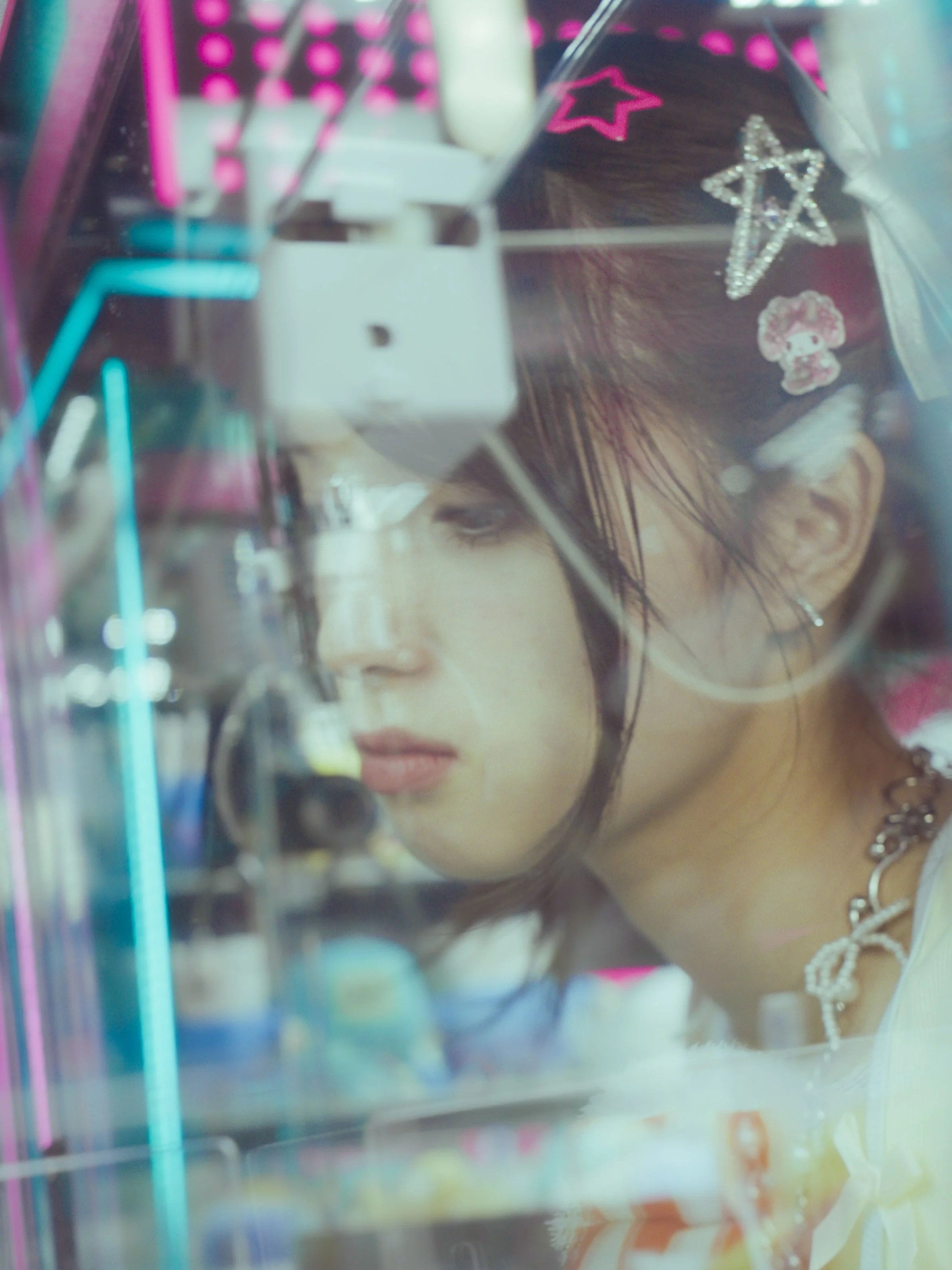 Close-up of a person's face with makeup, decorated with star-shaped and cartoon sticker accessories, wearing a necklace, and reflected on a shiny surface with bright pink, blue, and purple lights.