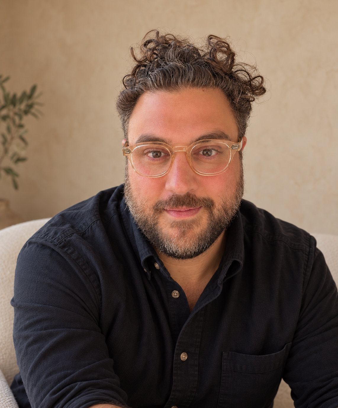Portrait of a bearded man with curly hair and clear-framed glasses wearing a black shirt.