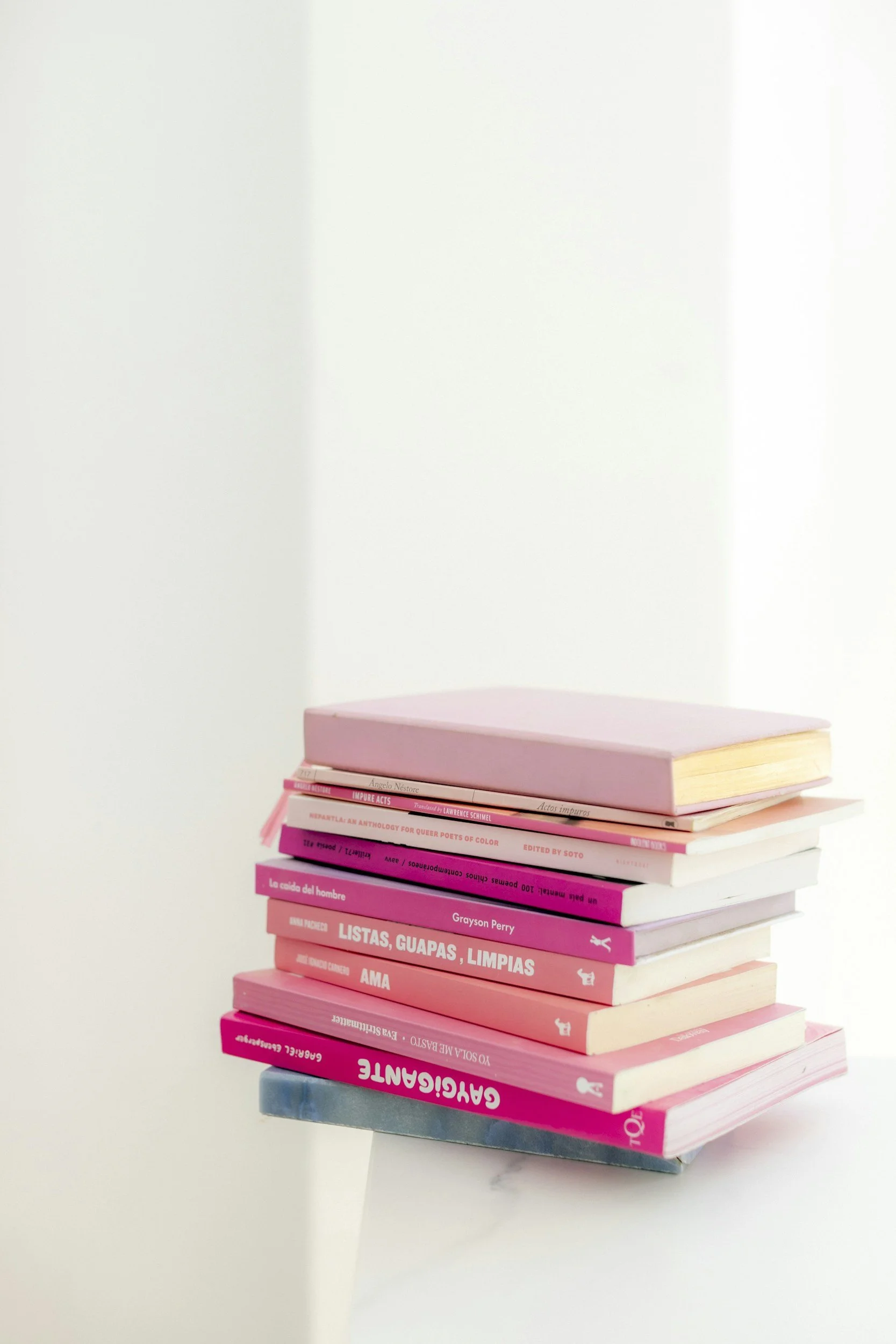 Stack of pink and white books on a white surface against a white background.