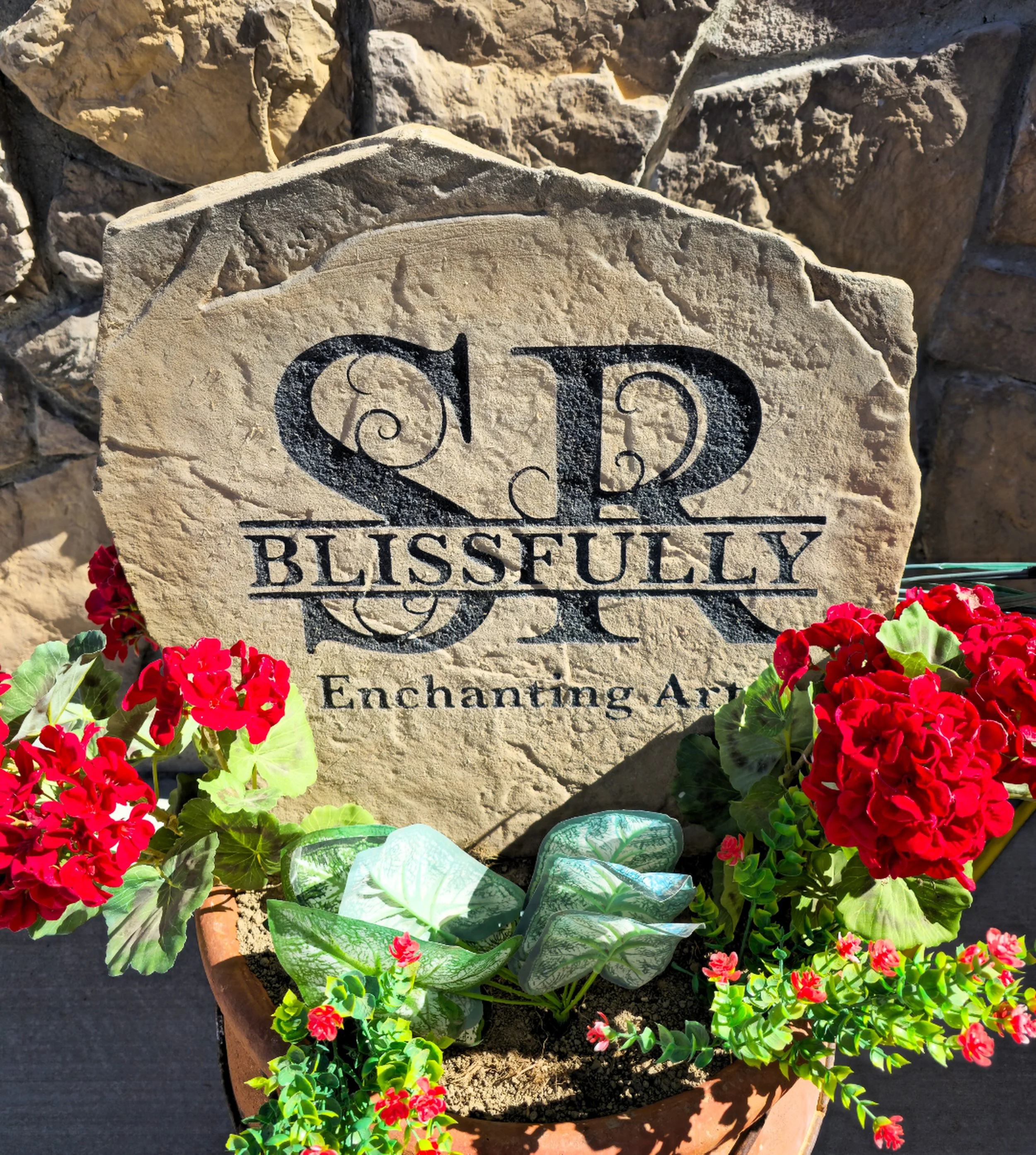 Close-up of a gravestone with the engraving 'In Loving Memory,' surrounded by vibrant red and green flowering plants.