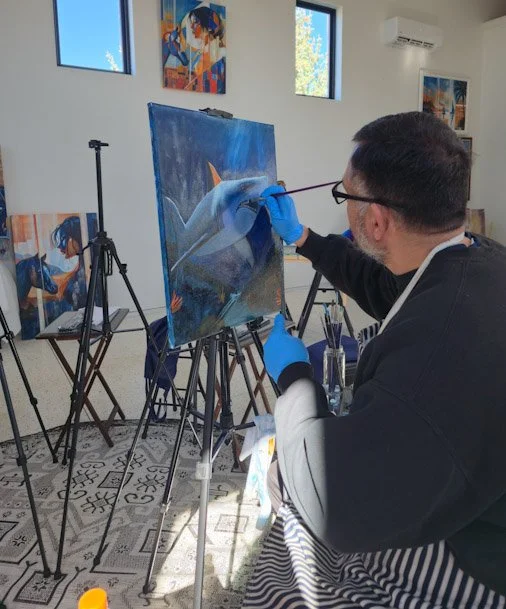 An artist painting a shark on a canvas in a well-lit art studio.