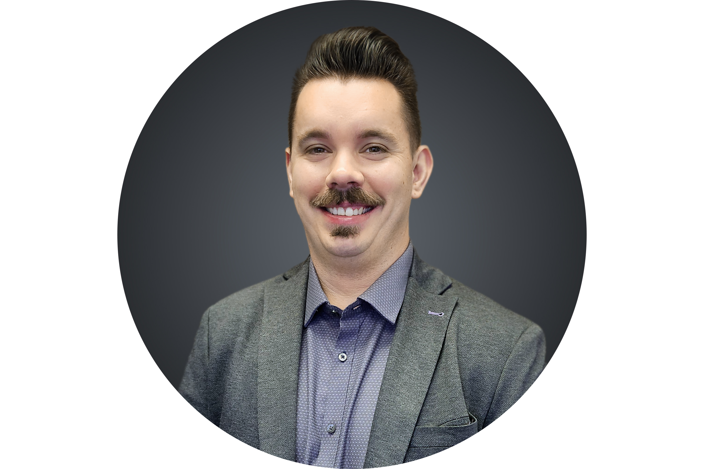 A smiling man with a mustache and goatee, wearing a gray blazer and a patterned shirt, standing against a dark background.